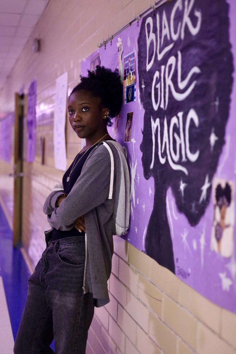 Planned Portrait, Superior: Black Girl Magic contest winner senior Sahara Cumberbatch stands in front of the “Black Girl Magic” billboard in the central hallway. She received her award from Tonya Moore on March 6 for the submission of her piece, “Women of Light and Color.” The contest was organized as part of the Black History Month event series at McCallum with the intention of highlighting Black female artists. Cumberbatch, won a coffee mug along with a $25 gift card. Cumberbatch’s winning submission was an art piece depicting a young Black woman empowered by her individuality. “I entered this piece because the inspiration was my identity as a Black girl, and because of that, the parts of me that make me stand out physically for most of my classmates,” she said. Cumberbatch hopes her piece will inspire confidence in embracing differences and emphasize the message that you don’t have to change the things that make you unique. “This year as a senior art major all my artworks have to connect in some way,” she said. “I’ve been exploring the struggles I faced with myself at times that up until now I usually try to ignore Cumberbatch viewed the contest as an opportunity to embrace her identity and show appreciation for Black History Month. She is especially thankful to contest organizer Tonya Moore, Students of Color Alliance sponsor, for encouraging her to submit her artwork to the contest. “Ms. Moore said that I should enter one of my art pieces. Because I’m a major, she thought It would be good to have one of my works,” she said. “I appreciate the chance for Black people and Black culture to be celebrated. Seeing the different submissions makes me smile whenever I walk in the hallways.”